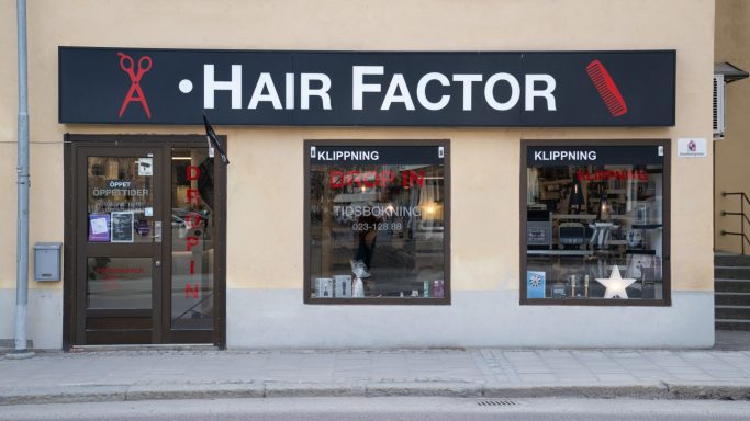 Framsidan av frisersalongen "Hair Factor" med skyltfönster och entré.